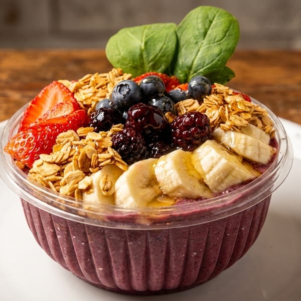 A vibrant acai bowl with granola, strawberries, blueberries, blackberries, bananas, and spinach.