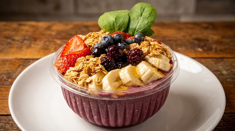 A vibrant acai bowl with granola, strawberries, blueberries, blackberries, bananas, and spinach.