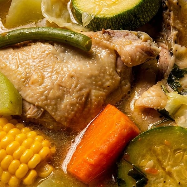 Hearty chicken soup with corn, zucchini, carrots, green beans, and chayote in a white bowl.