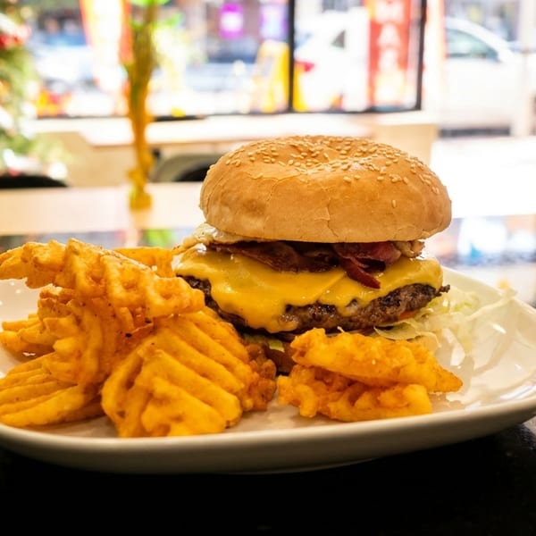 Cheeseburger with bacon and waffle fries on a white plate, with a blurred Christmas tree in the background.