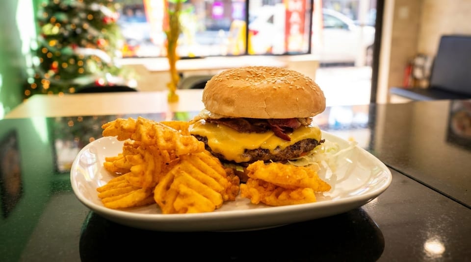 Cheeseburger with bacon and waffle fries on a white plate, with a blurred Christmas tree in the background.